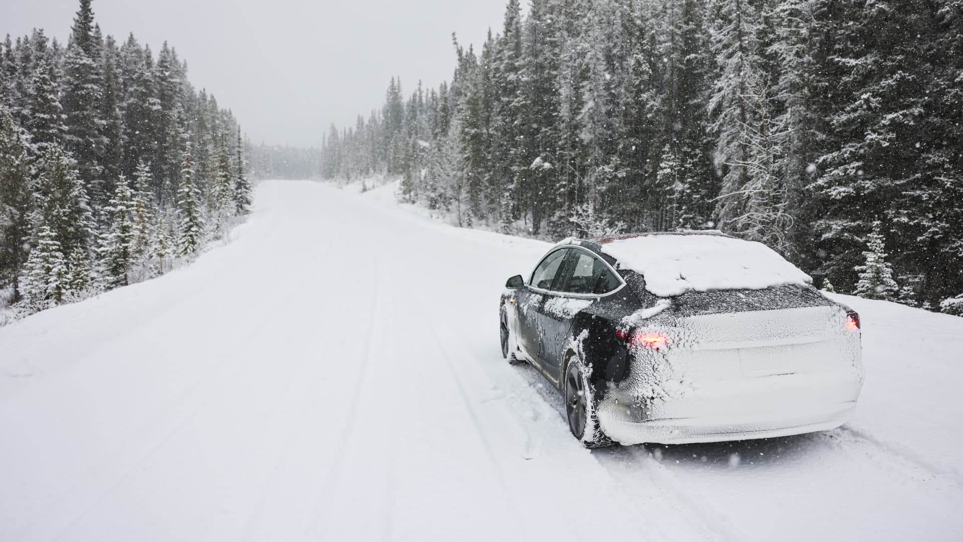 En elbil kör på en snöig väg genom en skog