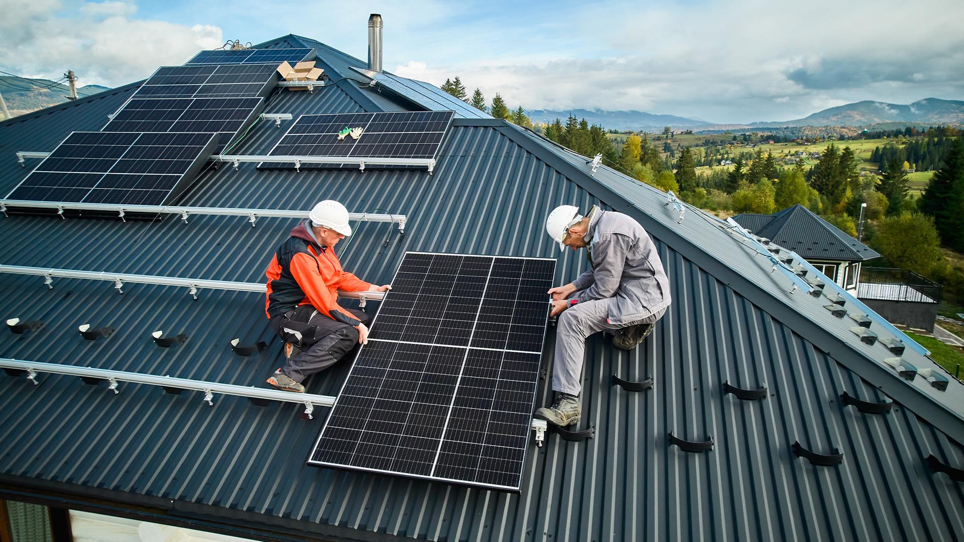 Två personer sätter upp solceller på ett tak.