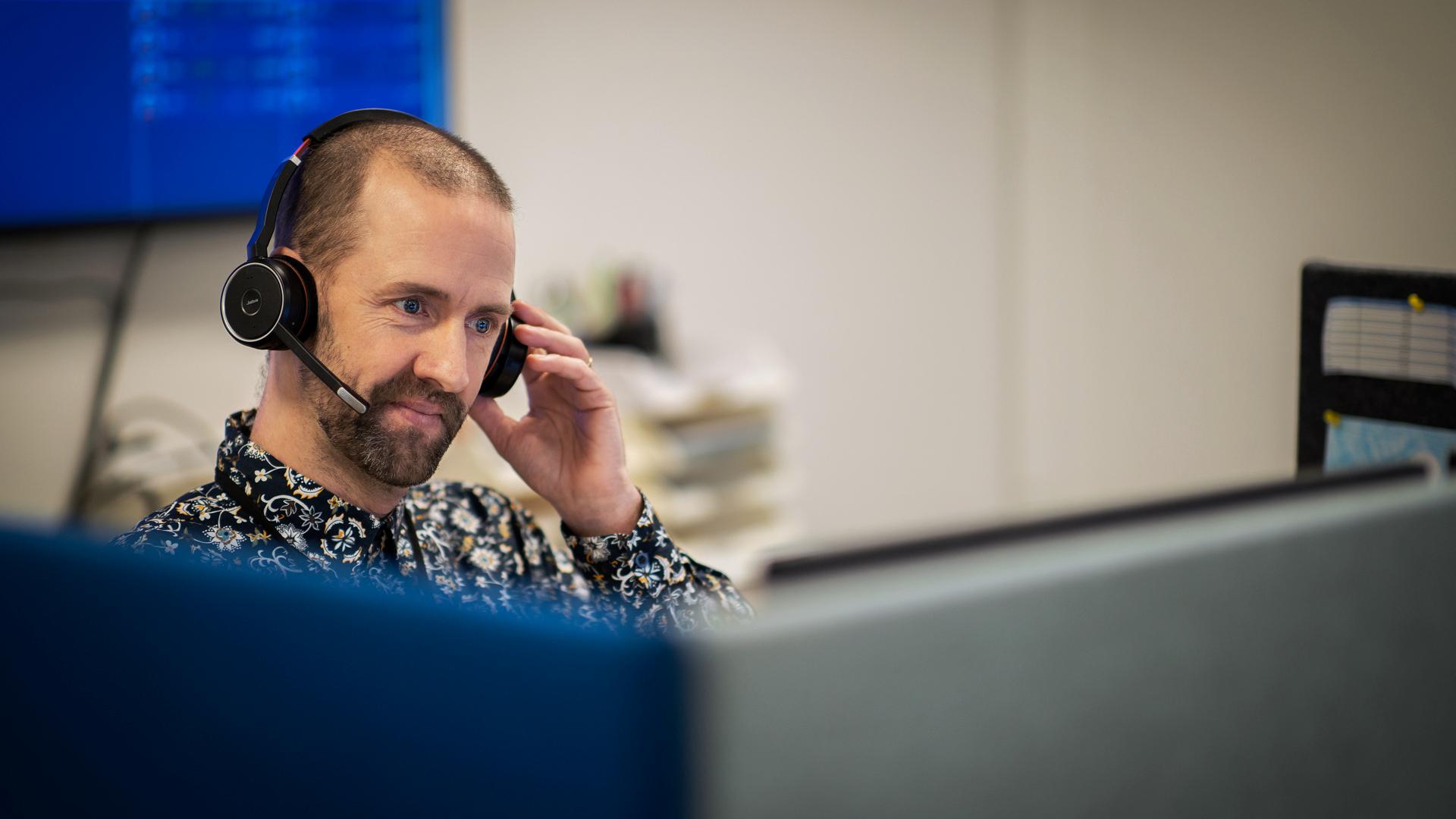 En medarbetare på Jämtkraft sitter med headset bakom ett par datorskärmar.