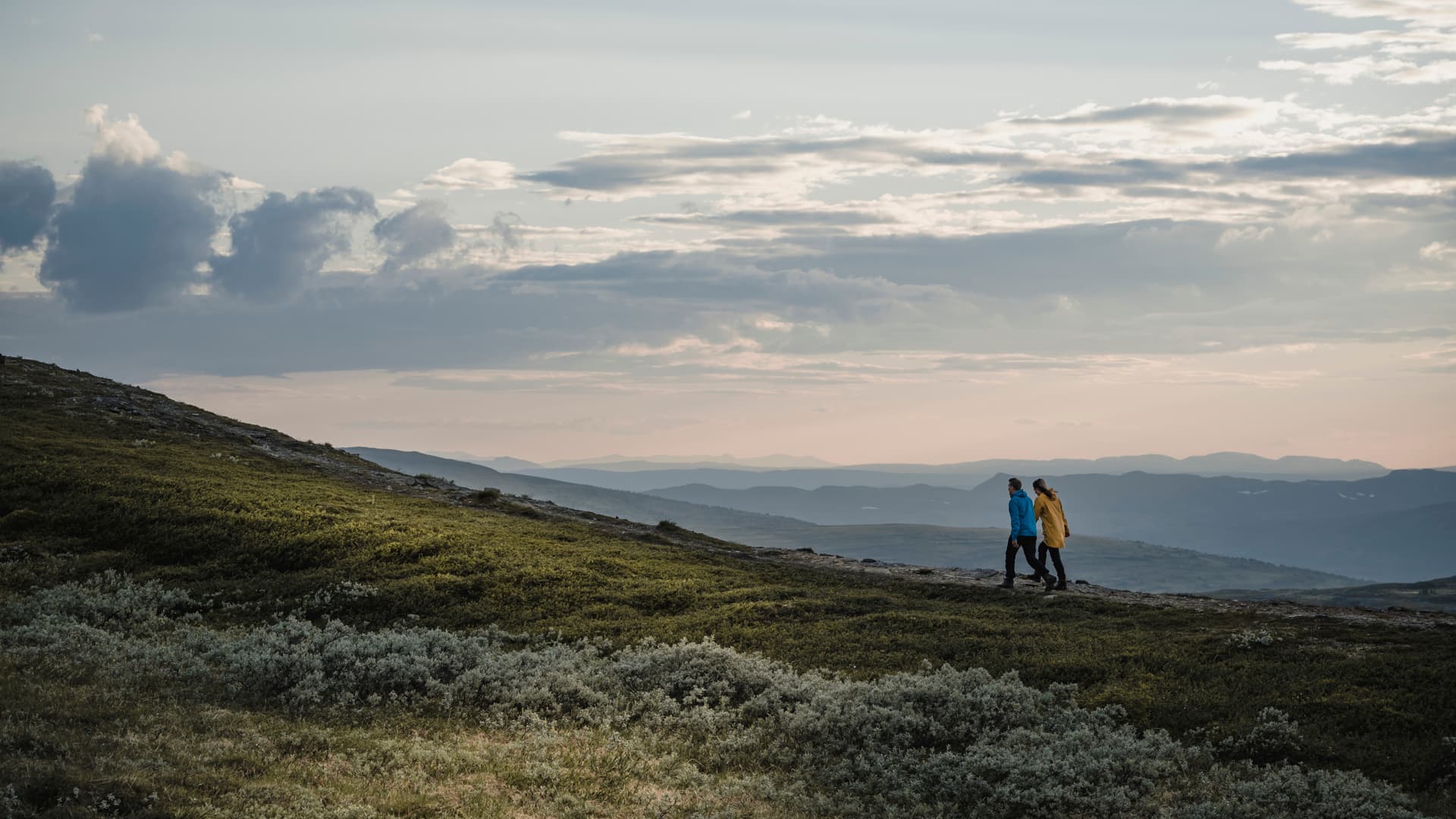Två personer vandrar på ett fjäll i skymning.