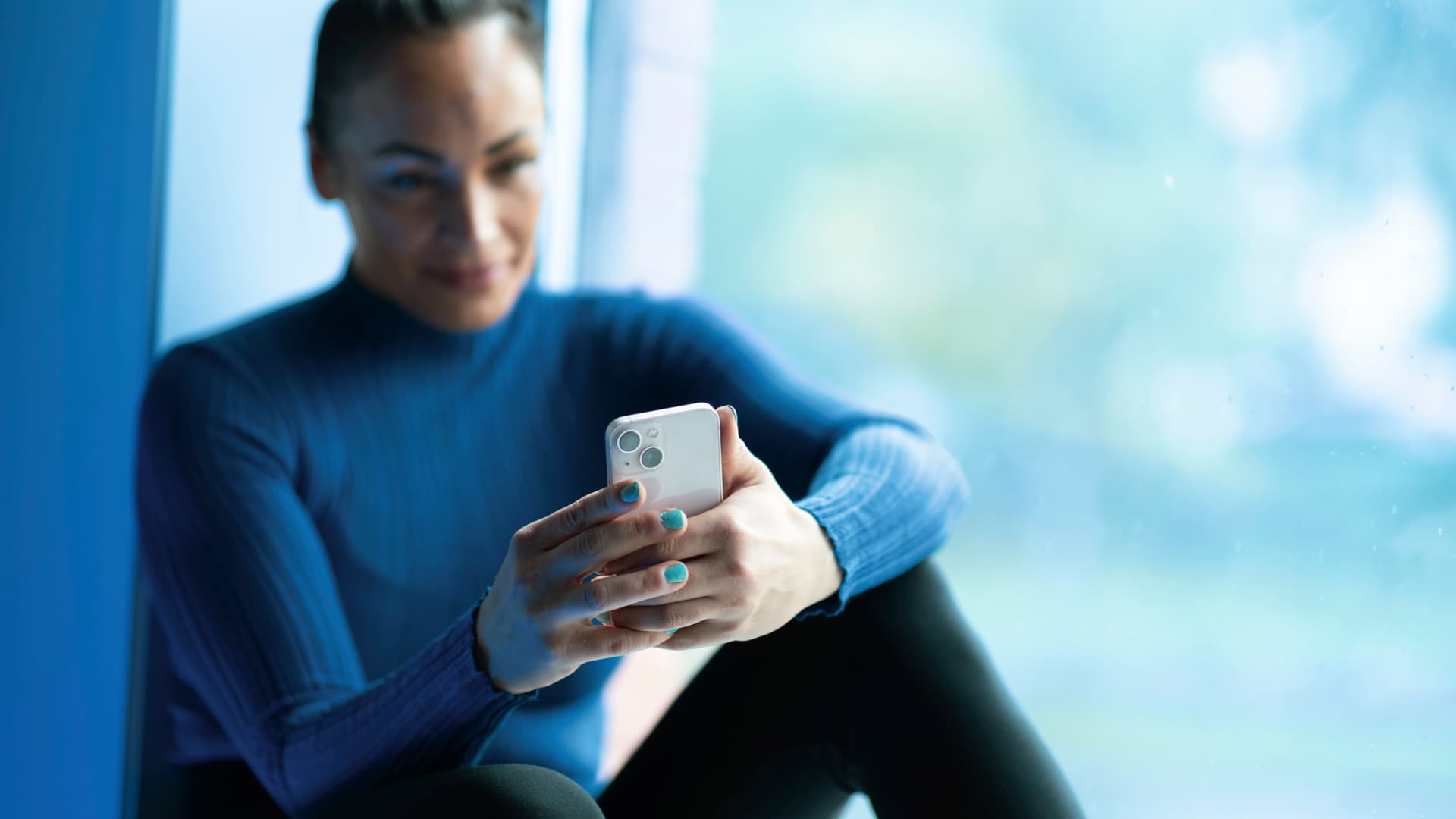 En kvinna sitter vid ett fönster med en mobiltelefon i händerna